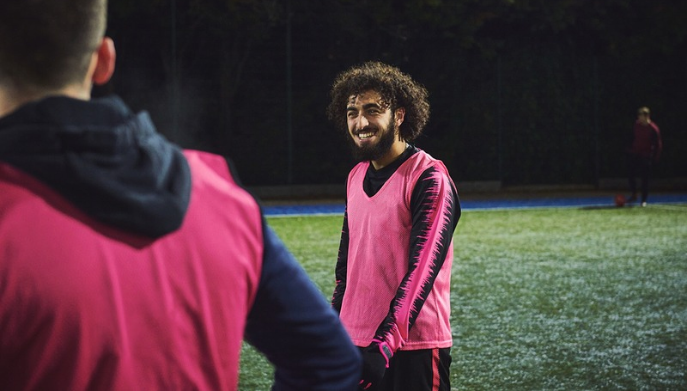 Participant in a pink training bib on a floodlit sports pitch during an evening team training session.