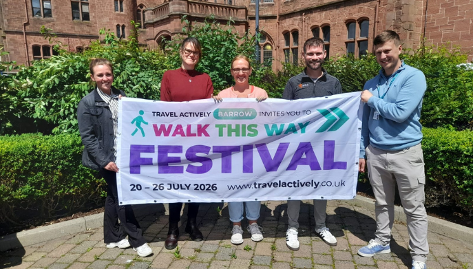 a group of adults standing outdoors holding an advertising banner for Walk This Way Festival