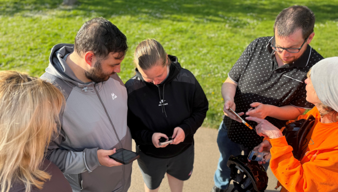 A group of adults standing outdoors looking at a mobile phone